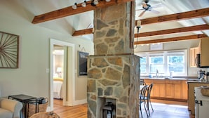 A spacious kitchen with a stone fireplace, wooden beams, and a view of the adjacent bedroom. - Firefly Cottage | Pet-Friendly, Fire Pit, 8 Mins to DT AVL + Biltmore Pass (Asheville)