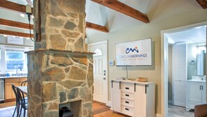 A stone fireplace, a kitchen with wooden beams, and a sign for Carolinamornings Luxury Vacation Rentals. - Firefly Cottage | Pet-Friendly, Fire Pit, 8 Mins to DT AVL + Biltmore Pass (Asheville)