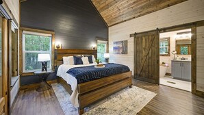 A bedroom with a large bed, wooden walls, a window, and a bathroom visible through an open door.