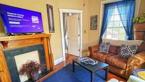 A living room with a fireplace, a television displaying a message, a brown leather sofa, and a blue carpet. - Nye's Place in Heart of Historic Roscoe Village (Coshocton)