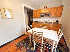 A dining area with a white table and chairs, wooden cabinets, a microwave, and a patterned rug. - Caroline`s Place in Historic Roscoe Village (Coshocton)