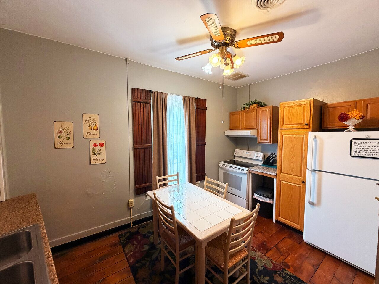 A compact kitchen with a dining table, wooden cabinets, a refrigerator, and a ceiling fan.