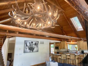 Un intérieur rustique agrémenté d’un lustre fait de bois de cerf, une cuisine avec des meubles en bois et un coin repas doté d’un bar.