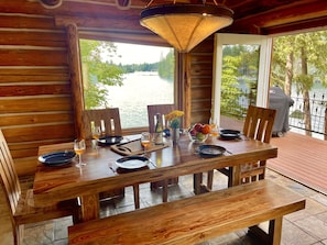 Une table de salle à manger en bois, dressée avec des assiettes, des verres et une bouteille de vin, donnant sur un lac.
