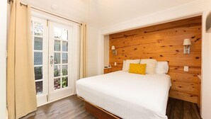 Une chambre à coucher avec une tête de lit en bois, un grand lit, une table de chevet et deux lampes fixées au mur.