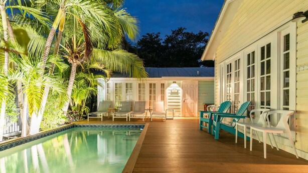 Un espace piscine doté d’une terrasse en bois, de chaises longues et d’un bâtiment avec de grandes fenêtres.
