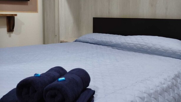A bed with a quilted mattress, a wooden headboard, and a folded towel on the bed. - Studio nearby Hospital and Train railway. (Livorno)