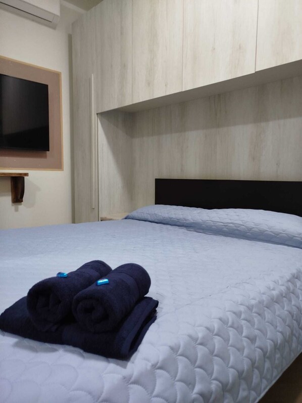 A bed with a quilted mattress, a wooden headboard, and a folded towel on the bed.