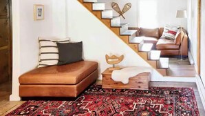 A room with a brown leather sofa, a patterned rug, a wooden chest, and a staircase leading to another room. - Never Lonesome Hunter: Smart 4bd Getaway near Mtn (Hunter)