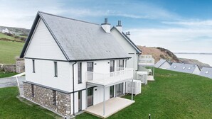 A two-story house with a balcony, stone foundation, and a view of the sea. - 2 Bed Ground Floor Apartment - 7 (Plas) (Gwynedd)