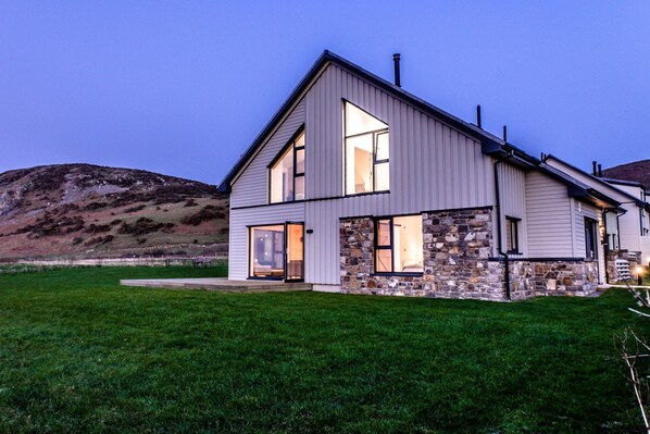 Une maison moderne à deux étages, dotée de fondations en pierre, de grandes fenêtres et d’une pelouse bien entretenue.