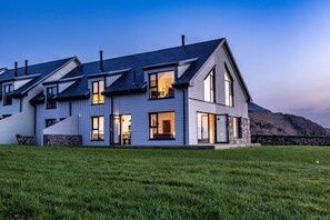 Une maison moderne à deux étages, dotée de grandes fenêtres, de fondations en pierre et d’une cour gazonnée.