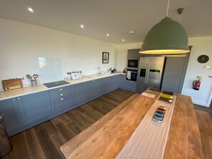 Une cuisine moderne avec des meubles gris, un îlot central en bois et un luminaire suspendu vert.
