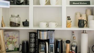 Una cocina con armarios blancos, diferentes equipos para preparar café y frascos de almacenamiento.