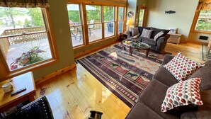 Un salon chaleureux avec une grande fenêtre, un plancher en bois, un canapé agrémenté de coussins à motifs et une tête de cerf fixée au mur.