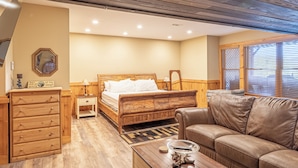 Une chambre à coucher avec un lit en bois, une commode en bois, un canapé en cuir et une fenêtre avec des stores.