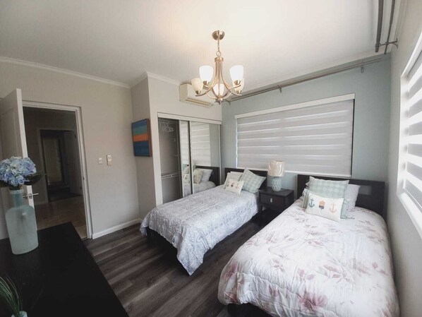 A bedroom with two beds, a chandelier, a closet, and a window with blinds.