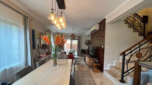 Amplia sala de estar con una larga mesa de comedor de madera, una escalera moderna y una cocina al fondo.