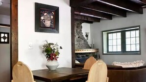 A dining area with a wooden table, chairs, a vase of flowers, a stone wall, and a window.