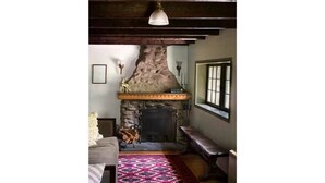 A cozy living room with a stone fireplace, a patterned rug, and a bench.