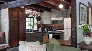 A cozy kitchen with wooden beams, a dining area with a table and chairs, and a sofa with a floral cushion.