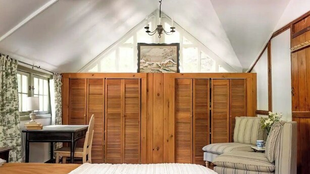 A bedroom with a bed, a desk, a chair, a sofa, and a wooden wardrobe.