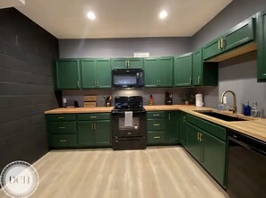 Une cuisine avec des meubles de rangement verts, une cuisinière noire et un four à micro-ondes.