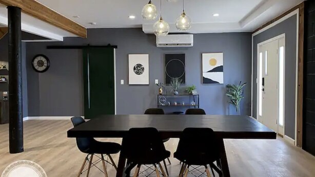 Uma área de refeições moderna com uma mesa comprida, cadeiras pretas e iluminação pendente.