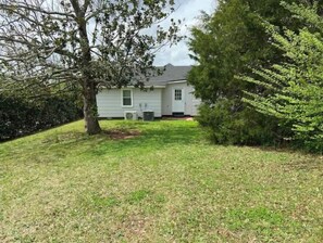 Enjoy a peaceful stay in this single-story house with a gabled roof and front porch, surrounded by a well-maintained lawn and trees.