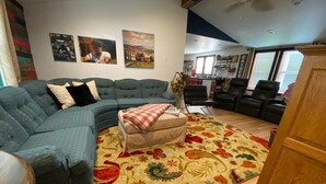 Una sala de estar con un sofá seccional, un pequeño reposapiés, un tapete floral y un mueble de madera.