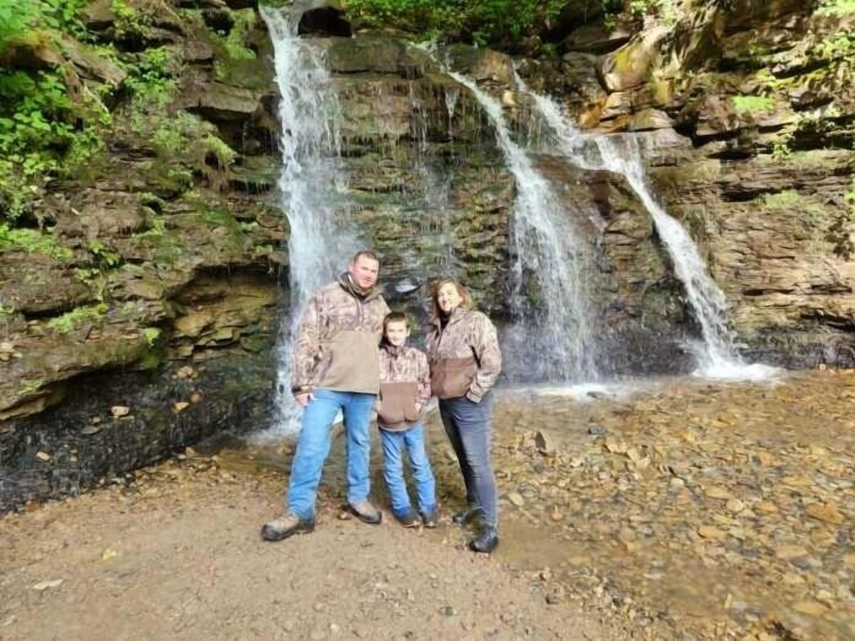 A family standing in front of a waterfall with rocky terrain and greenery.