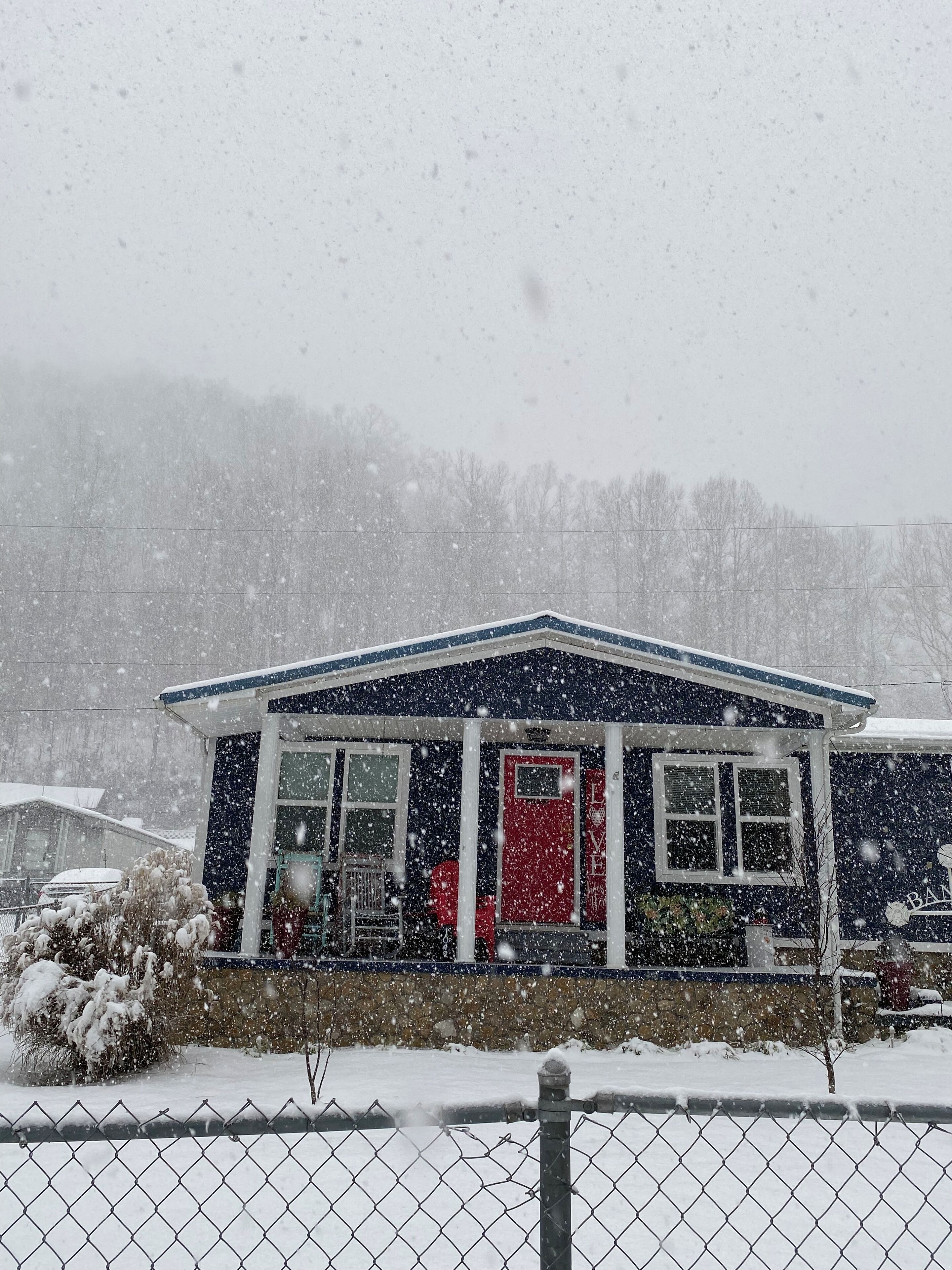Ein Haus mit roter Tür, einer Veranda und einem schneebedeckten Vorgarten.