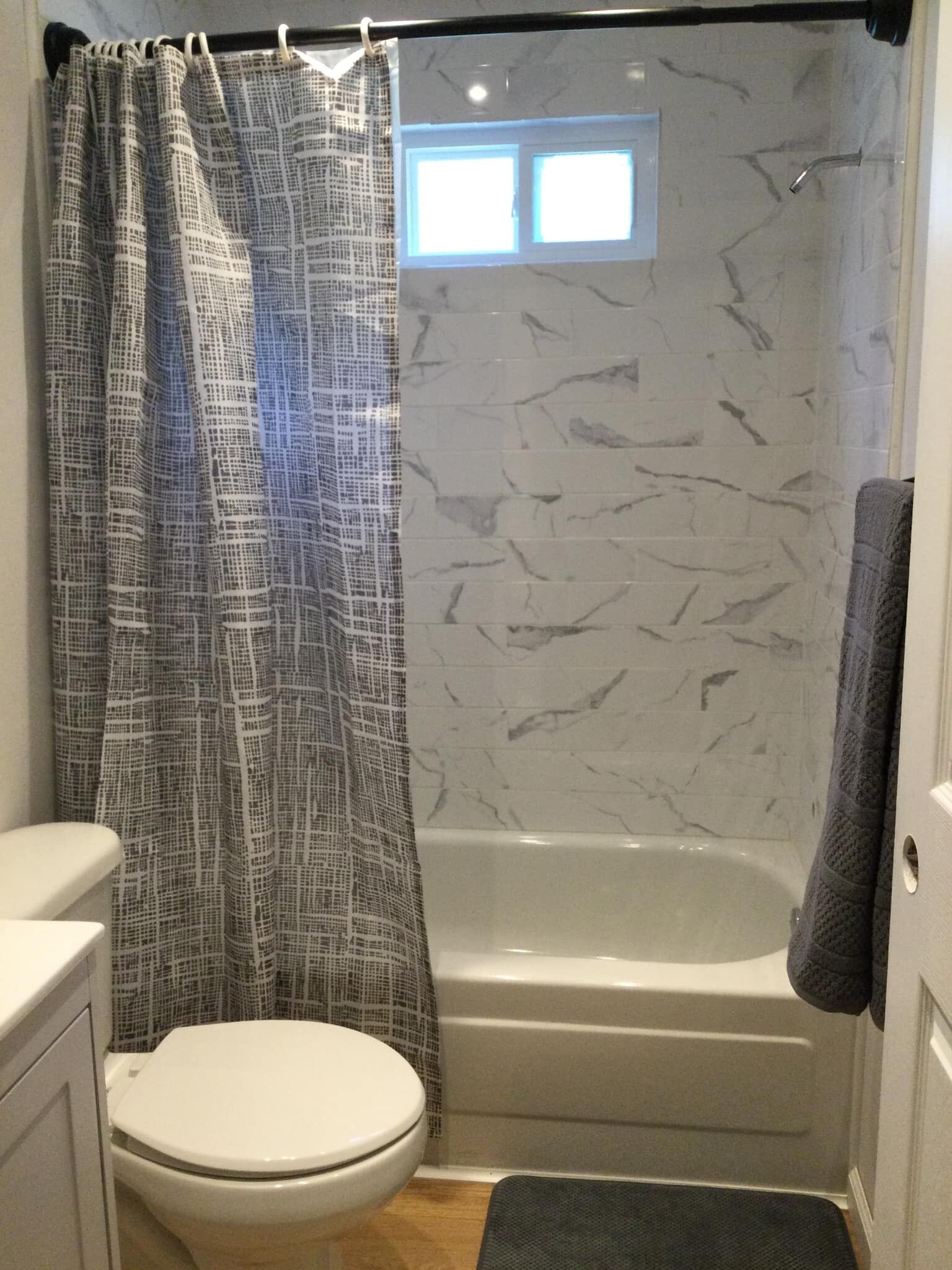 Un bagno con un WC bianco, una doccia con tenda a quadri e un muro in marmo.