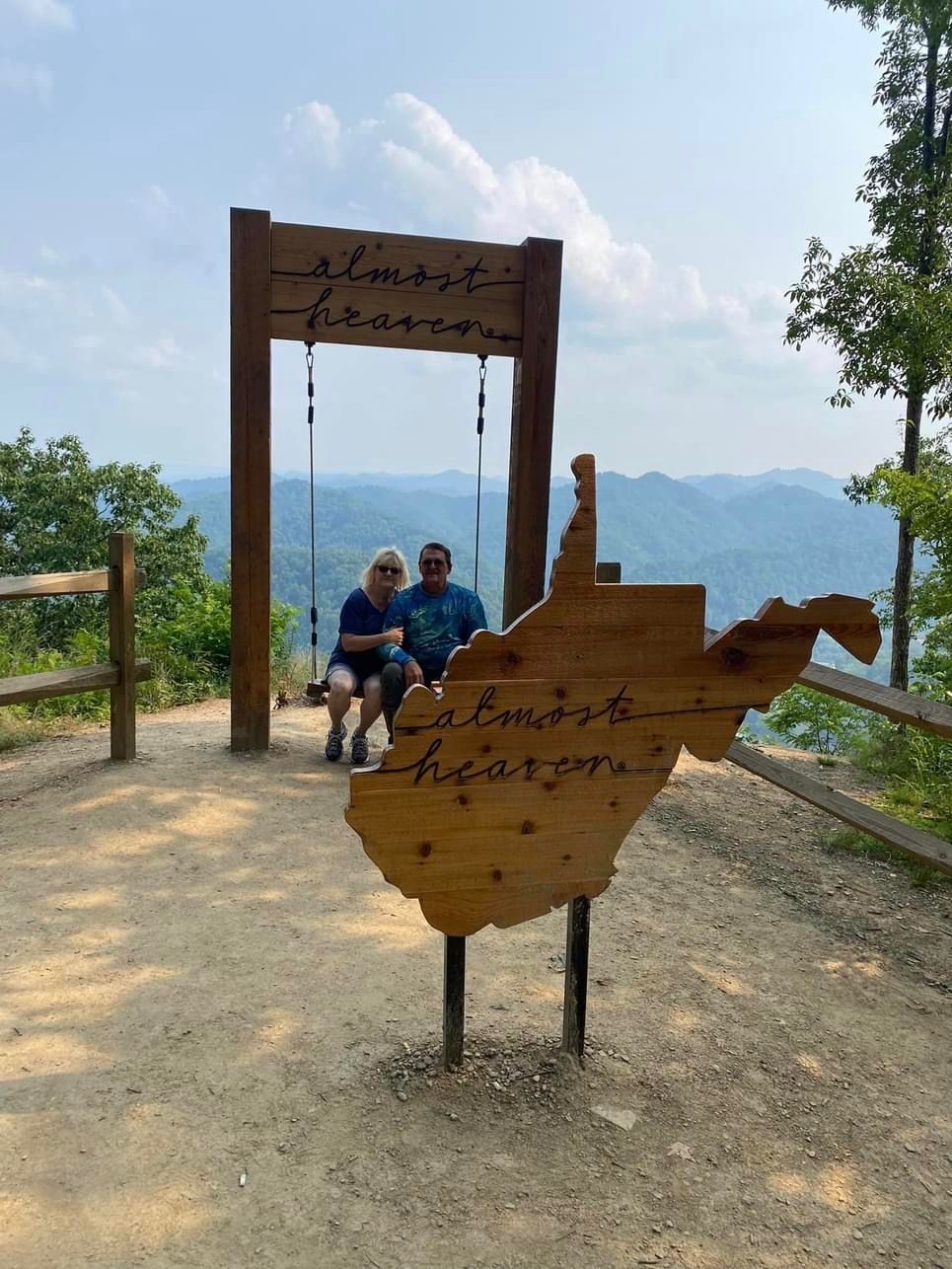 A wooden sign with the words 'almost heaven' and a swing set with two people.