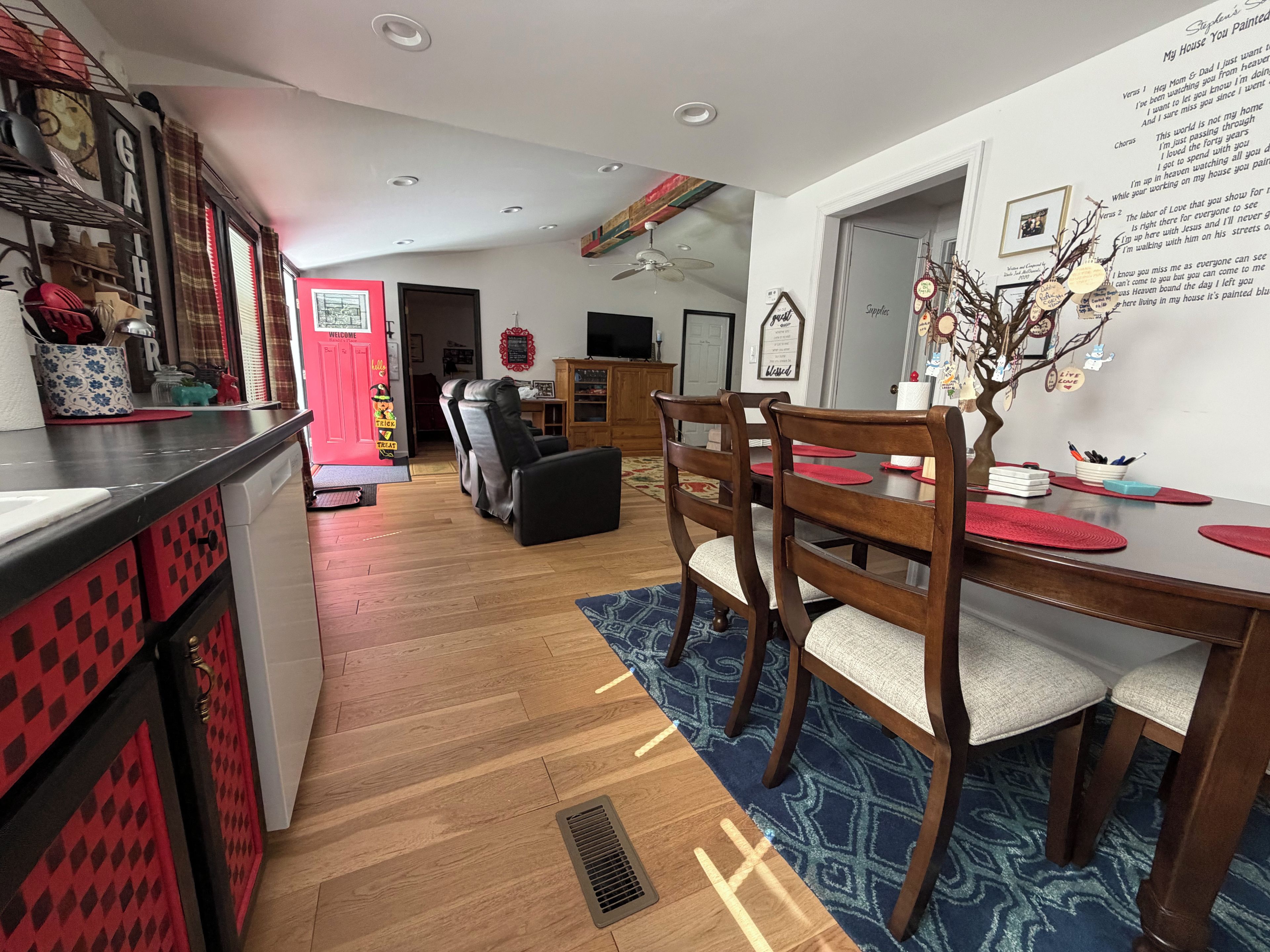 Une cuisine moderne aux couleurs rouge et noir, un coin repas avec des chaises et une table en bois, et un salon avec un canapé et un téléviseur.