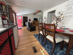 A modern kitchen with a red and black color scheme, a dining area with wooden chairs and a table, and a living room with a sofa and a television.