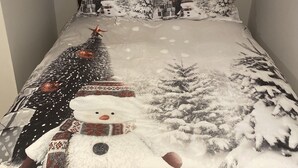 Una cama con edredón de temática invernal que muestra muñecos de nieve y árboles de Navidad.