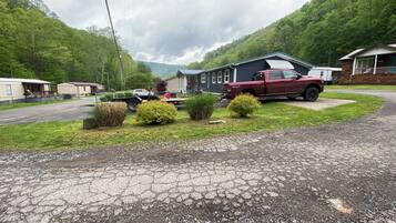 A residential area with a red truck parked in front of a house, a driveway, and a grassy area with bushes.