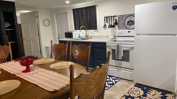 A compact kitchen with a dining table, chairs, a refrigerator, and a microwave.