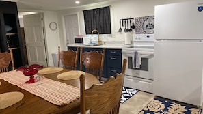 A compact kitchen with a dining table, chairs, a refrigerator, and a microwave.