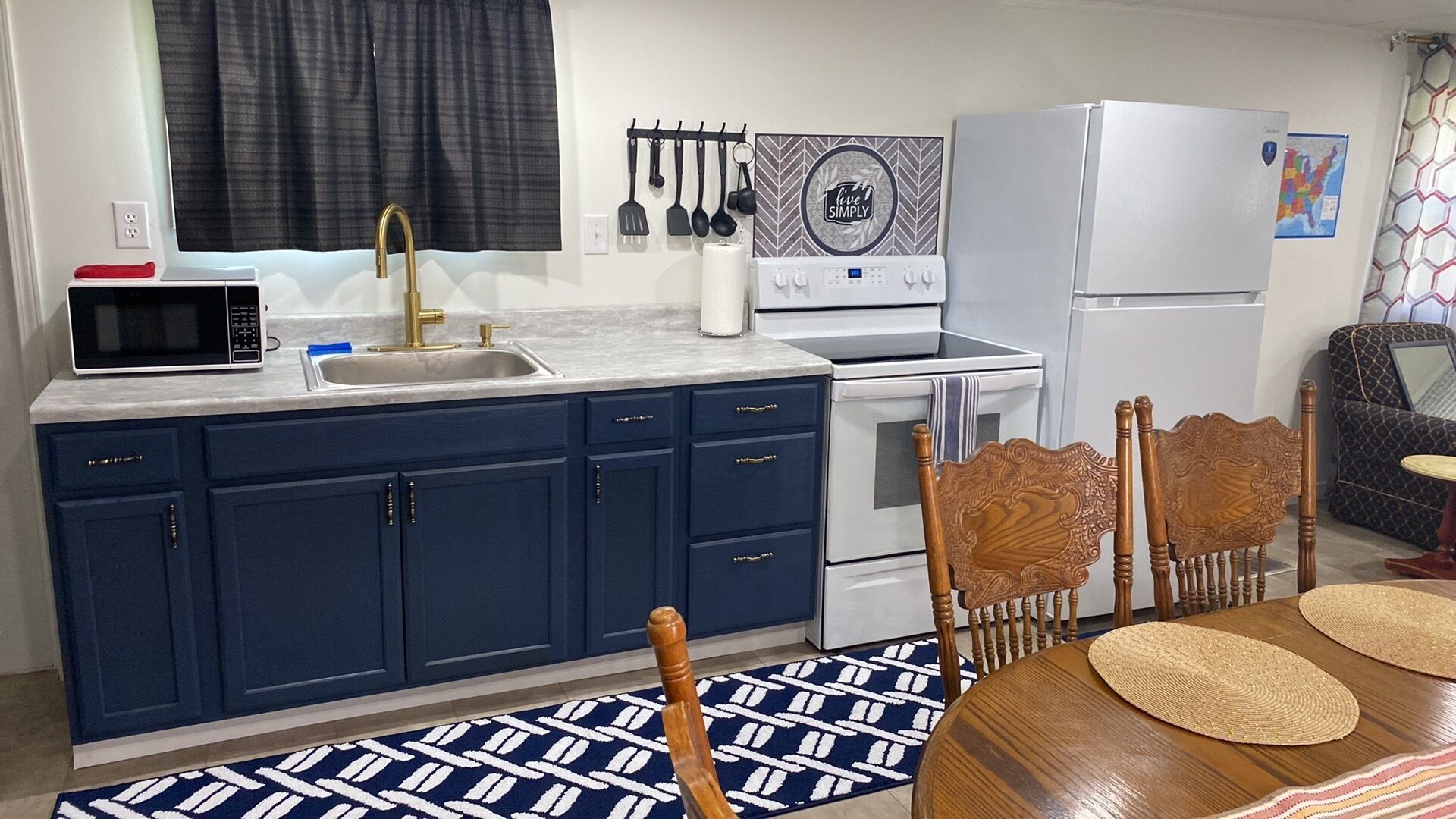 A compact kitchen with a microwave, sink, and stove. There are cabinets, a chair, and a dining table with placemats.