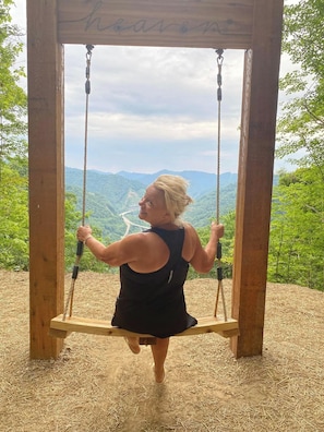 A person on a wooden swing with a view of a valley and mountains in the background.