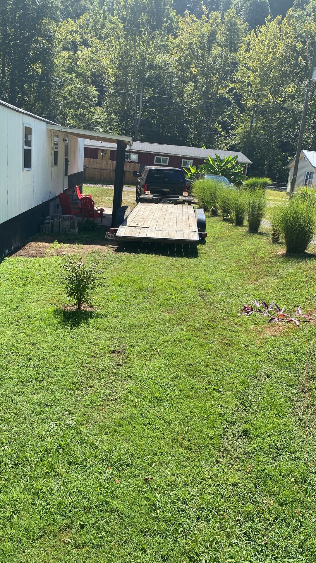 A residential area with a trailer, a vehicle on a trailer, and a small tree.