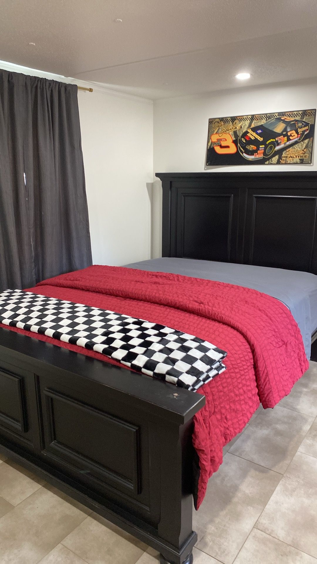 Un dormitorio con cama, cabecera, colcha a cuadros, manta roja y decoración en la pared.