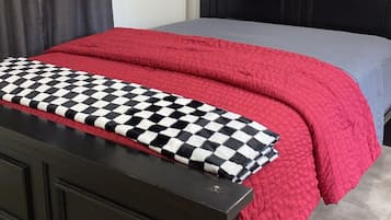 Un dormitorio con cama, cabecera, colcha a cuadros, manta roja y decoración en la pared.