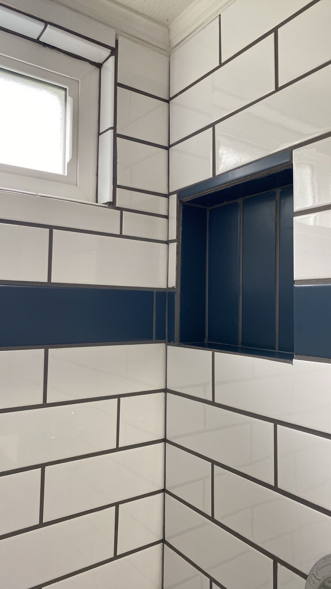 A corner of a room with white and dark blue tiles, a window, and a door.