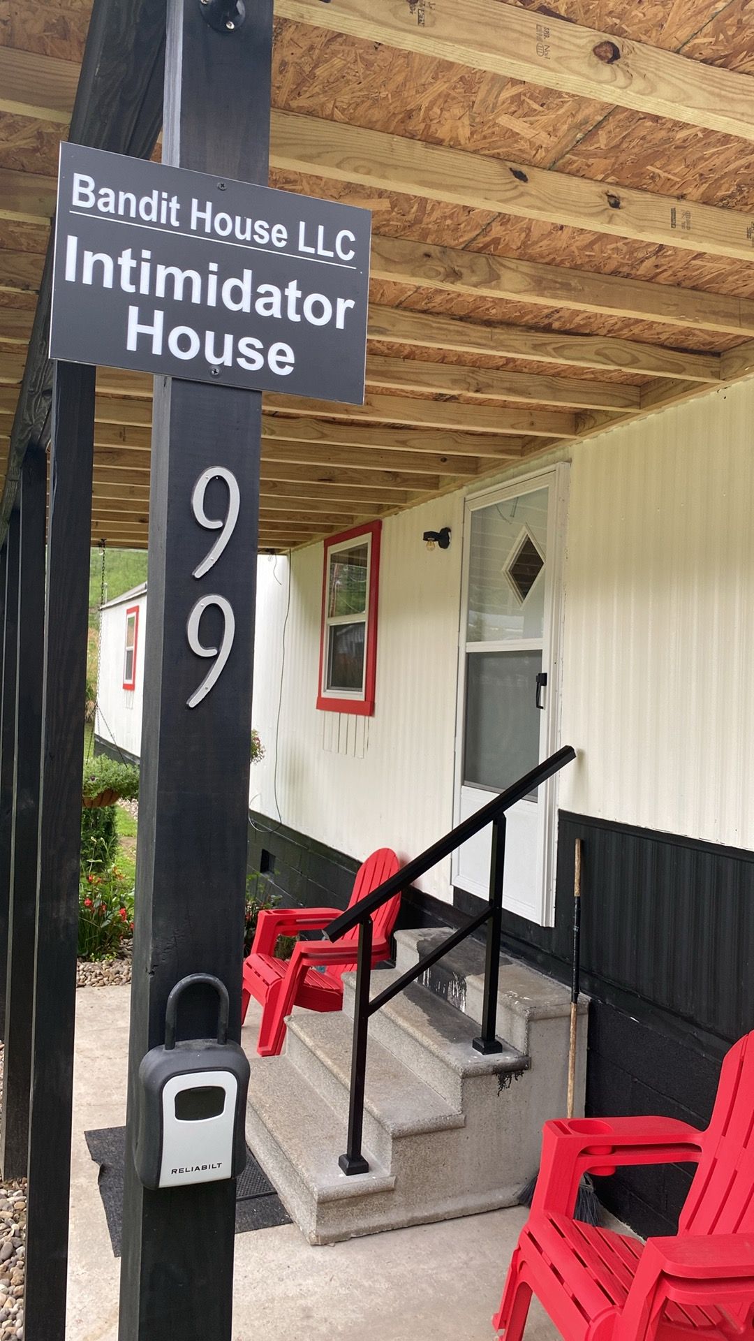 A wooden porch with a sign for Bandit House LLC, a staircase, and red chairs.