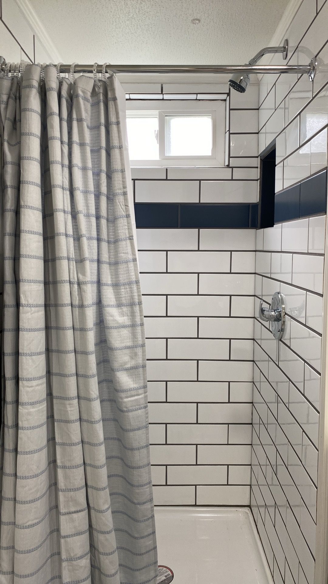 A bathroom with a shower area, white tiled walls, and a striped shower curtain.