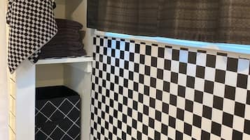 A bathroom with a checkered tile backsplash, a towel rack with a patterned towel, and a green bottle on a shelf.