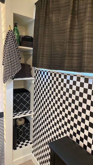 Une salle de bain avec un mur recouvert de carreaux à motifs, un porte-serviettes orné d’une serviette à motifs et une bouteille verte posée sur une étagère.